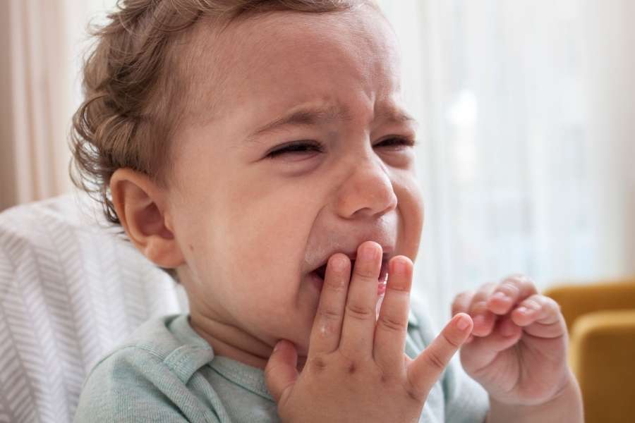Un bébé qui pleure et met ses doigts dans sa bouche à cause d'une poussée dentaire douloureuse.