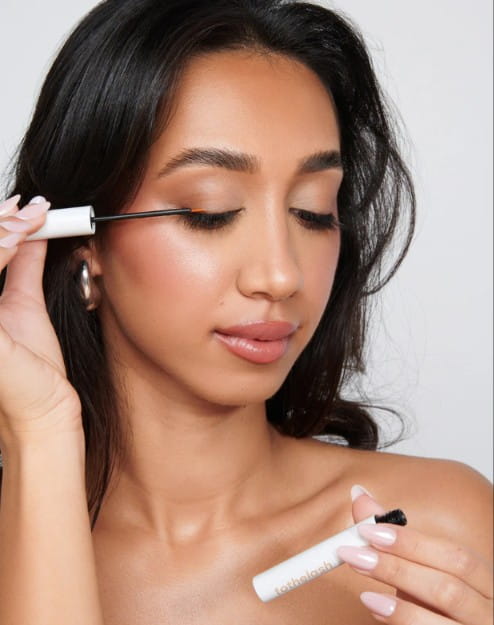Une femme brune applique délicatement un sérum pour les cils à la racine de ses paupières à l'aide d'un applicateur fin.