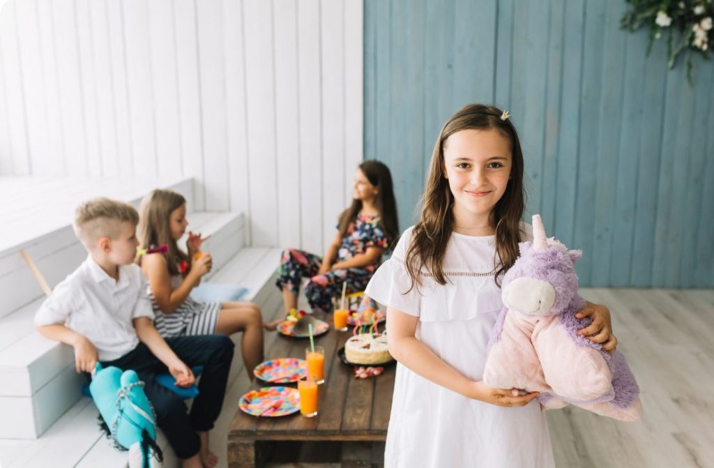 Petite fille souriante tenant une peluche licorne dans un espace dédié grâce aux idees animations et baby-sitter enfants mariage.