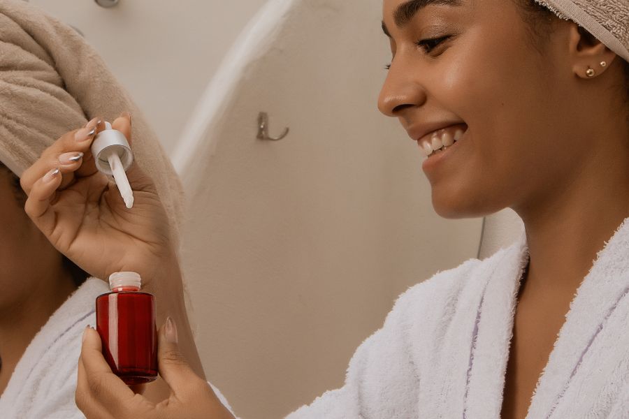 Une femme souriante en peignoir tient un flacon de sérum avec une pipette compte-gouttes.
